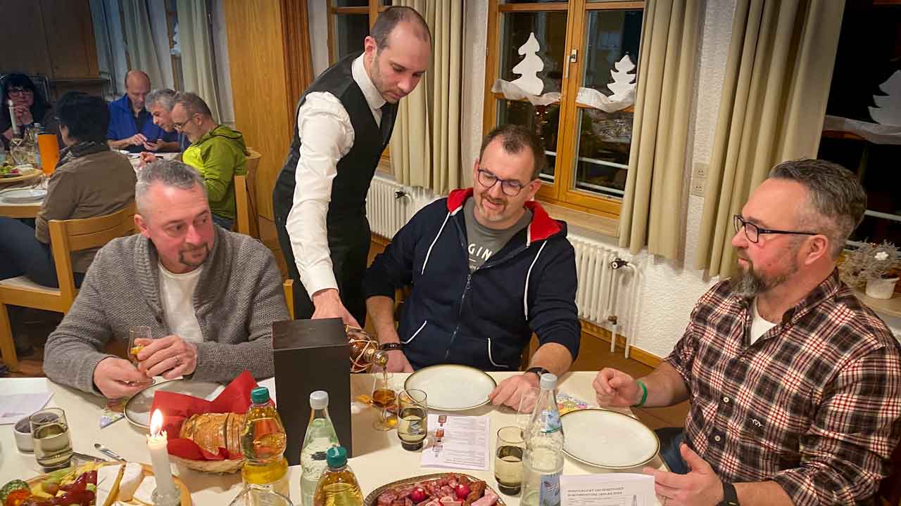 3 Männer sitzen am Tisch, der Kellner schenkt Rum ein.