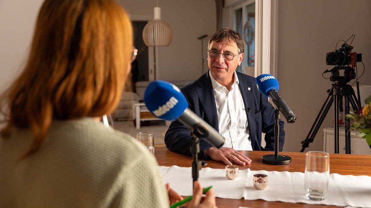 Kirchenpräsident Volker Jung sitzt am Tisch mit einem Mikrofon vor sich. Er nimmt gemeinsam mit Lotte den indeon-Podcast „echt gefragt - der Deeptalk“ auf.