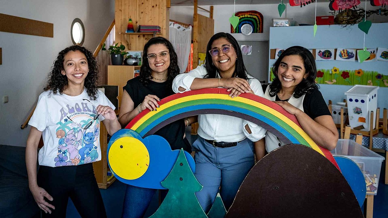Vier Erzieherinnen aus Kolumbien in den Kita-Räumen fotografiert, vor ihnen ein Regenbogen aus Holz
