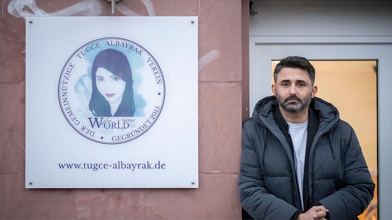 Dogus Albayrak steht neben dem Schild des Vereins „Tugce Albayrak“.