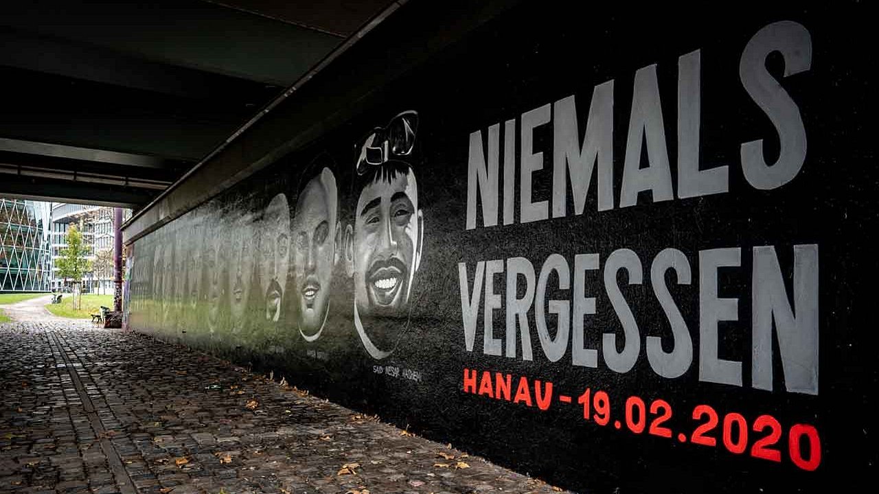 Das Graffito in Frankfurt am Main zum Gedenken an die Opfer des rassistischen Mordanschlags vom 19. Februar 2020 in Hanau. Es zeigt von links nach rechts die Gesichter der neun Ermordeten, Fatih Saracoglu, Vili Viorel Paun, Kaloyan Velkov, Ferhat Unvar, Mercedes Kierpacz, Gökhan Gültekin, Sedat Gürbüz, Hamza Kurtovic und Said Nesar Hashemi. Die Porträts und die Worte „Rassismus tötet“ erstrecken sich über die gesamte Länge der Friedensbrücke.