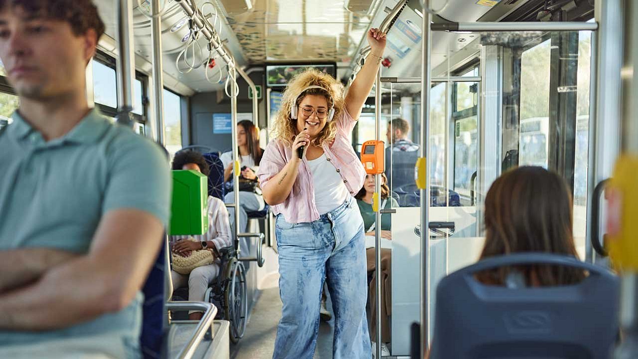 Sorglose übergewichtige Frau, die Spaß beim Musikhören und Tanzen während einer Fahrt im Bus hat.