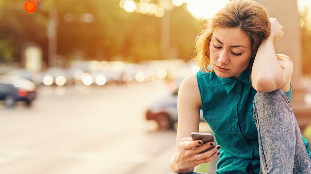 Junge Frau, die sich von ihrem Freund trennt, während sie auf einer Brücke in der Nähe des großen Boulevards sitzt. Freizeitkleidung mit Hemd und Jeans.