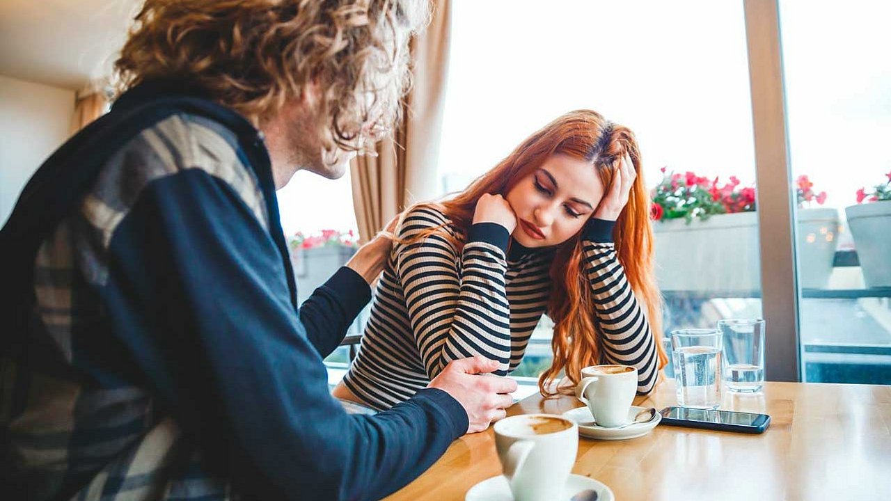 Heterosexuelles Paar sitzt im Cafe, sie sieht traurig aus, er tröstet sie