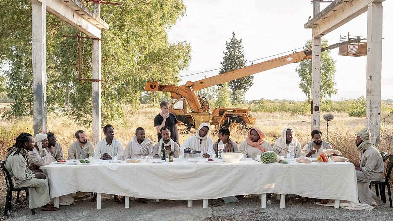 Eine lange weiße Tafel, im Hintergrund erkennt man einen Kran und dadurch die laufenden Filmaufnahmen