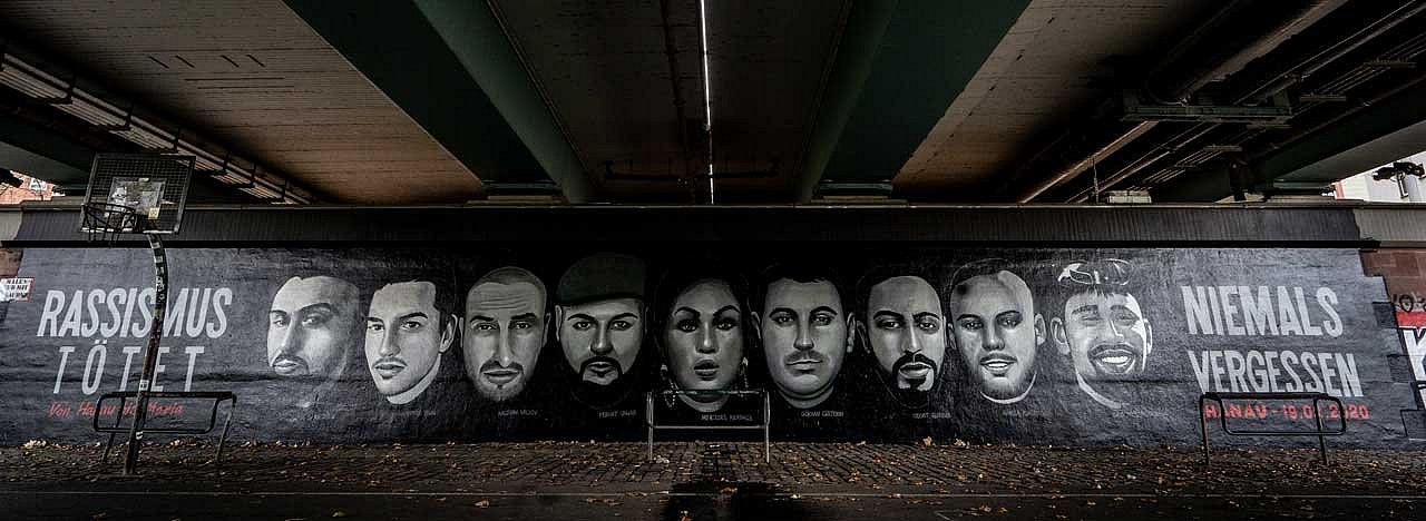 Das Graffito in Frankfurt am Main zum Gedenken an die Opfer des rassistischen Mordanschlags vom 19. Februar 2020 in Hanau. Es zeigt von links nach rechts die Gesichter der neun Ermordeten, Fatih Saracoglu, Vili Viorel Paun, Kaloyan Velkov, Ferhat Unvar, Mercedes Kierpacz, Gökhan Gültekin, Sedat Gürbüz, Hamza Kurtovic und Said Nesar Hashemi. Die Porträts und die Worte „Rassismus tötet“ erstrecken sich über die gesamte Länge der Friedensbrücke.