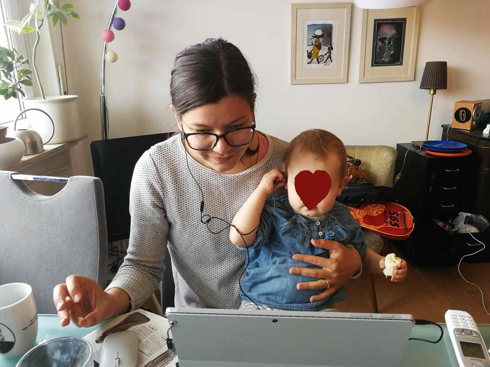 Charlotte Mattes mit Tochter auf dem Schoß, Blick auf dem Bildschirm. Beide haben Stöpsel im Ohr zum Telefonieren.