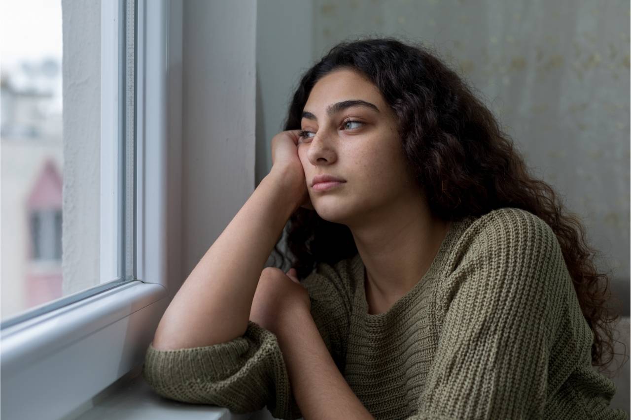 Eine Jugendliche sitzt am Fenster und schaut traurig hinaus